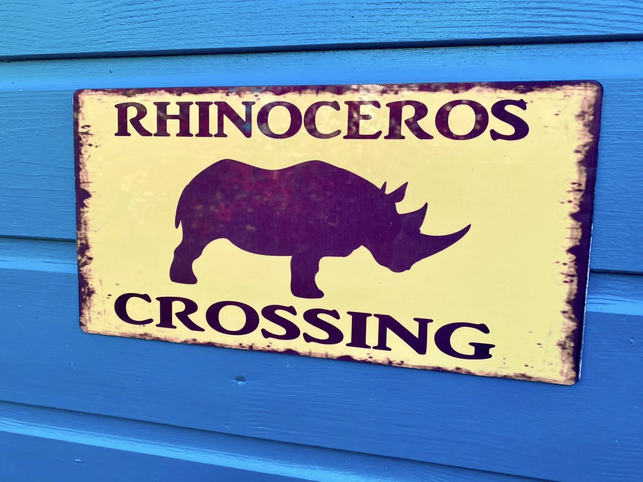 Sign with a silhouette of a rhinoceros, reading 'Rhinoceros Crossing', mounted on a blue wall.