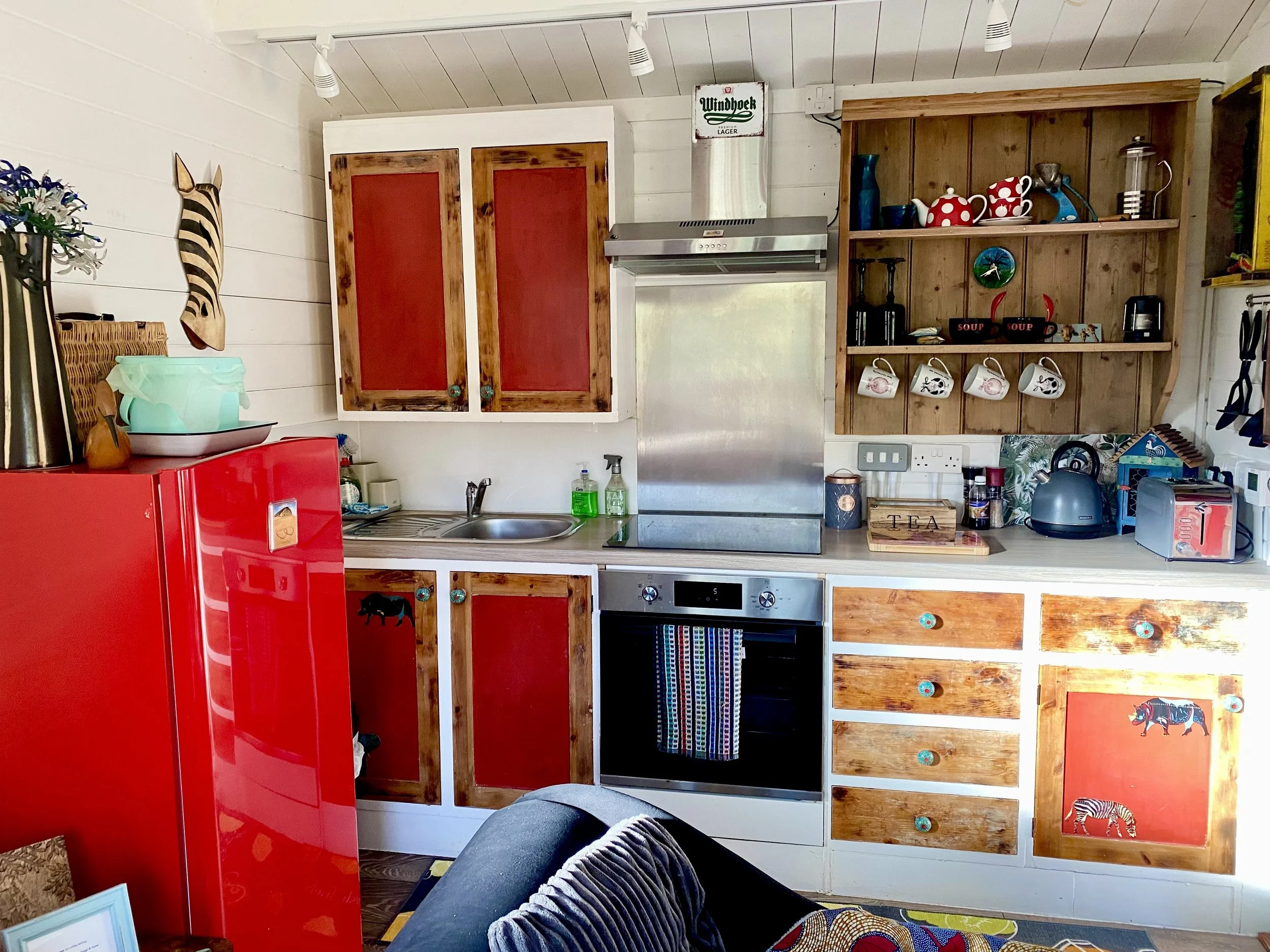 The kitchen in the self-catering chalet Little Africa, there is a two-seater sofa, a chaise lounge and a small kitchen with fridge, stove, oven, sink and kettle