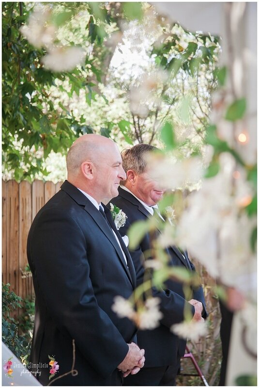  groom and best man framed by flowers at the altar 