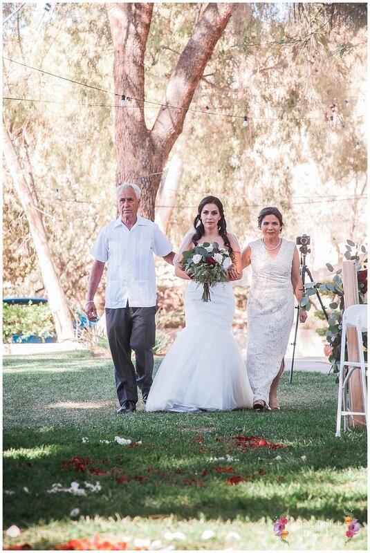  bride walks down the ranch aisle with mother and father 
