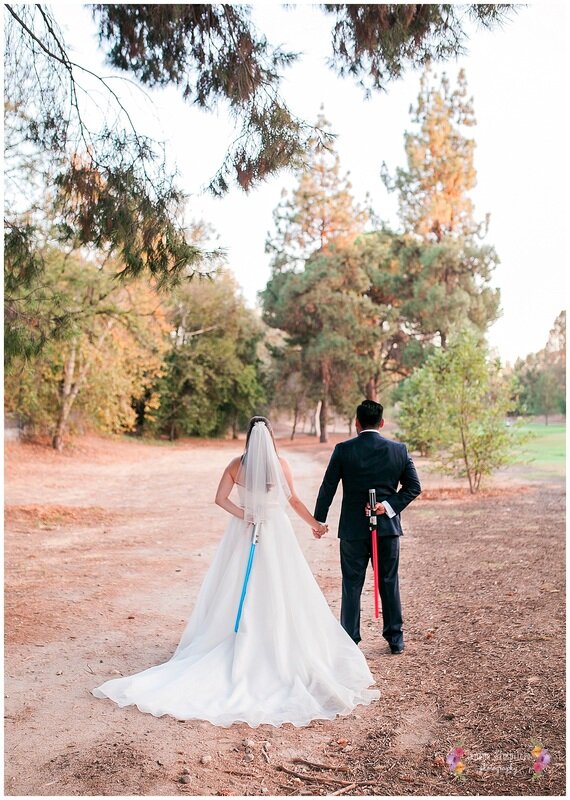  bride and groom hand in hand with light sabers behind their back 