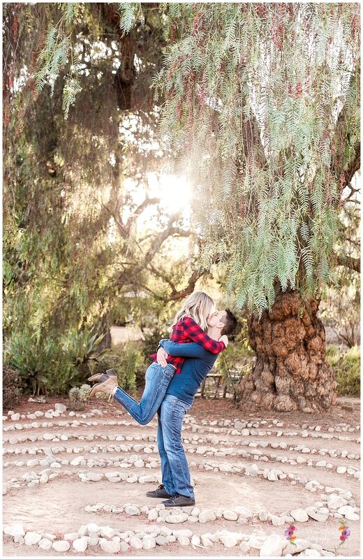  groom to be lifting up  his bride with a kiss in the middle of a circular rock garden 