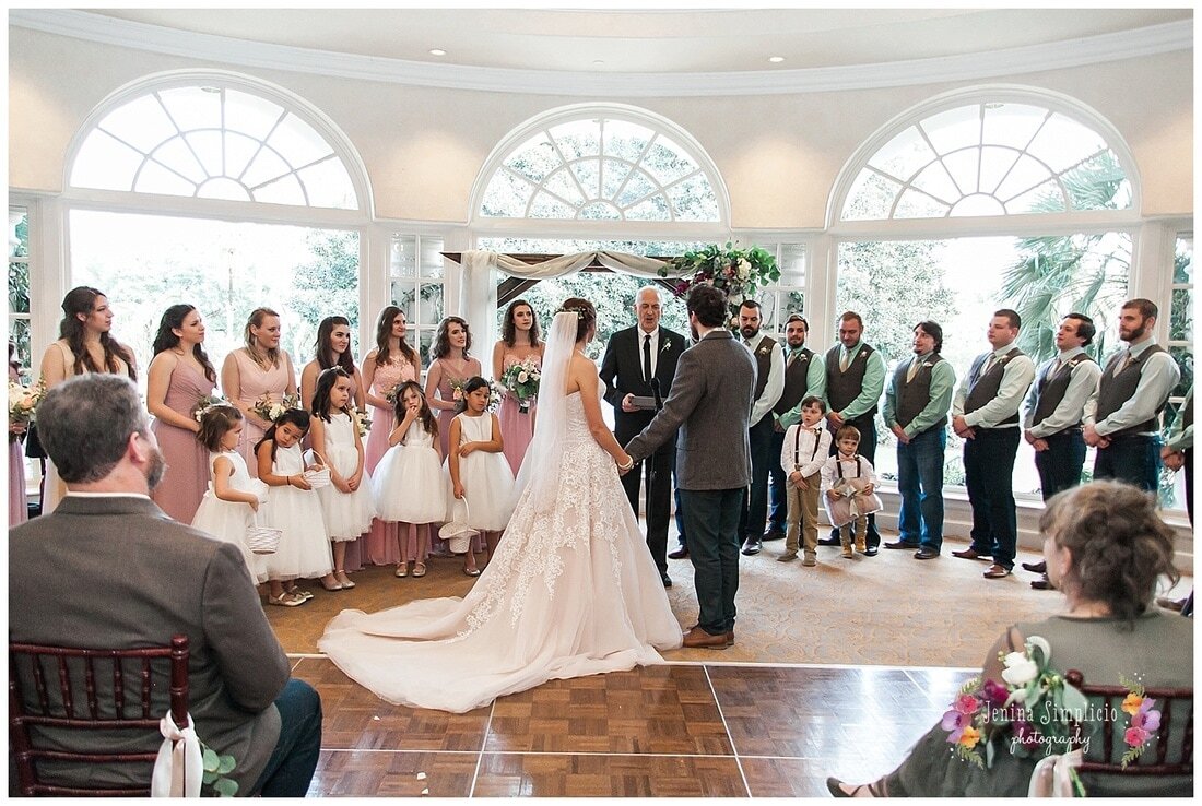  full wedding party at the ceremony in front of huge windows 