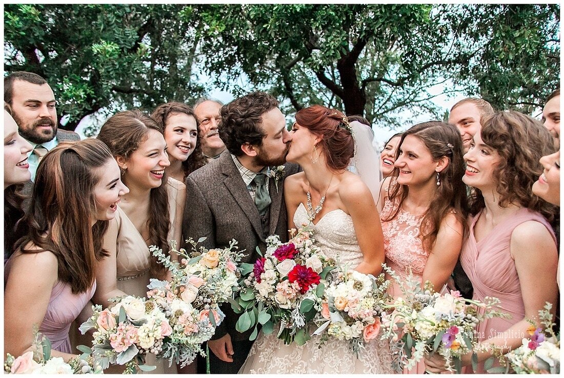  bride and groom kiss surrounded by their wedding party  