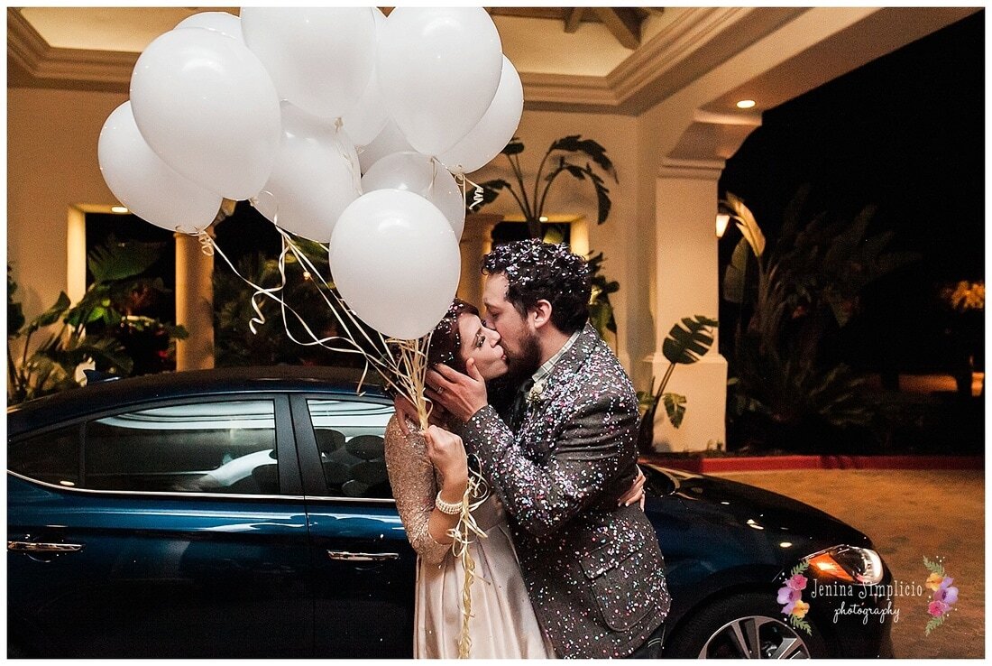  bride and groom holding balloons covered in confetti kissing 