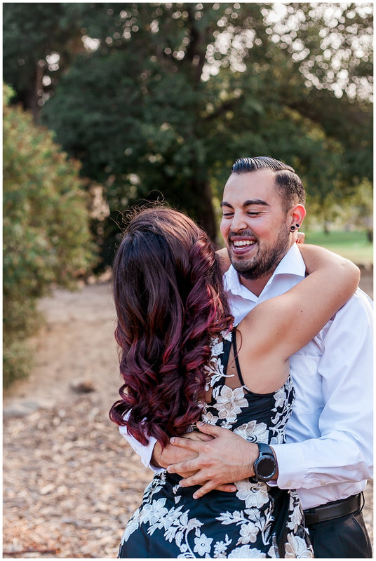  bride to be’s hair drapes down her back and groom laughs as they embrace one another 
