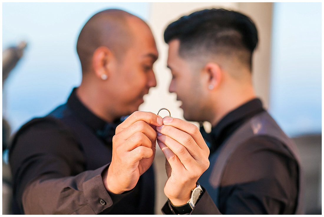  grooms holding the engagement ring and looking to one another behind it 