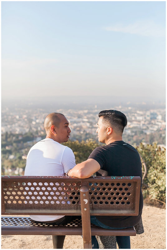  grooms to be sit on a park bench looking out over los angeles at sunrise 