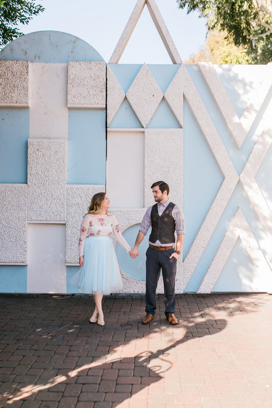  newly engaged couple holding hands in front of a blue and white wall mural 
