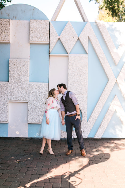  newly engaged couple kissing in front of a blue and white wall mural 