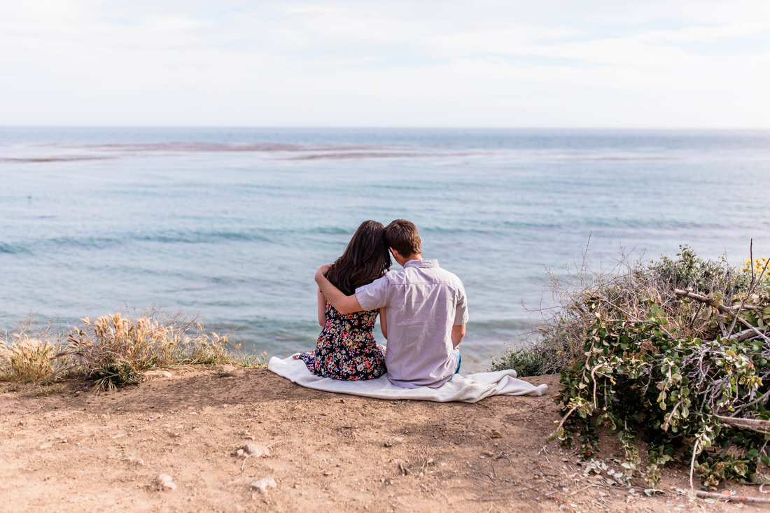  couple holding one another and sitting on the beach looking out at the ocean 