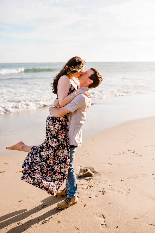  groom lifts his bride up to kiss her on the beach 