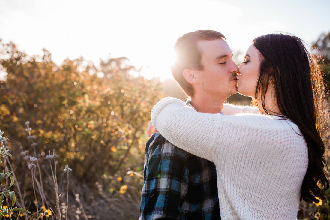  bride and groom with their arms wrapped around one another kiss in the field of flowers by the beach dunes 