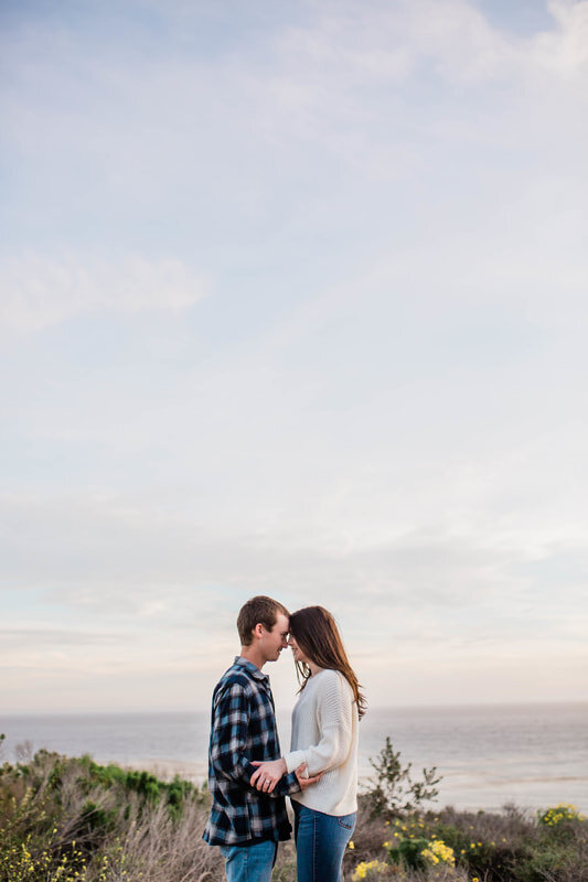  couple touching foreheads with the ocean behind them 