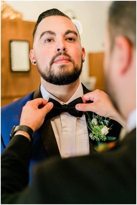  best man helping to straighten out the groom’s bow tie 