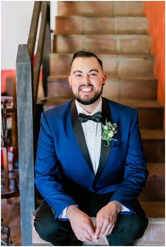  groom smiles and sits on the stairwell in the groom’s suite 