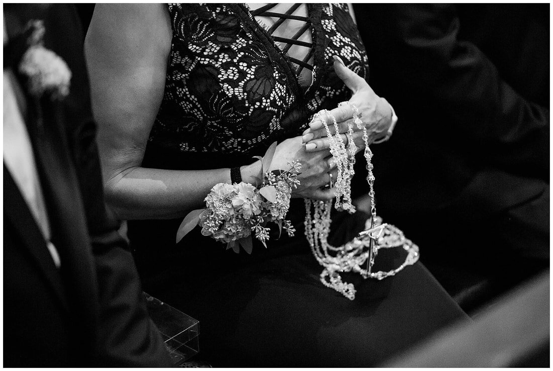  mother of the bride holding rosery beads in her hands while sitting in the pews 