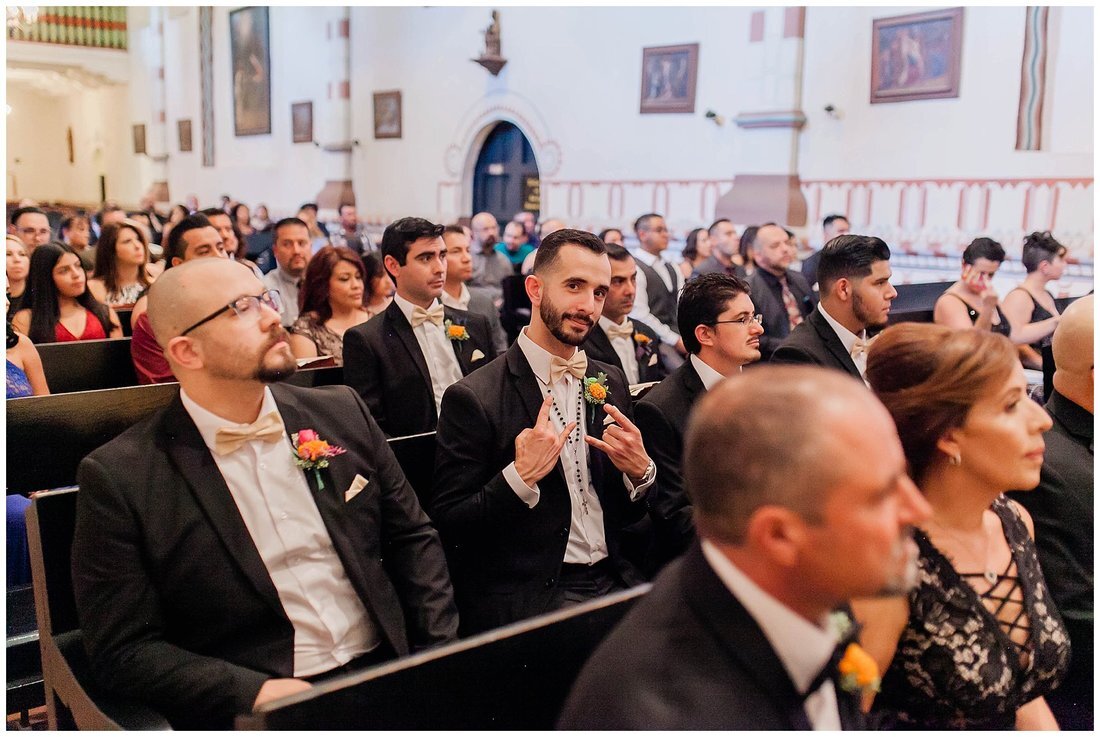  groomsmen make a rock on sign surrounded by other guests in the pews of the church 