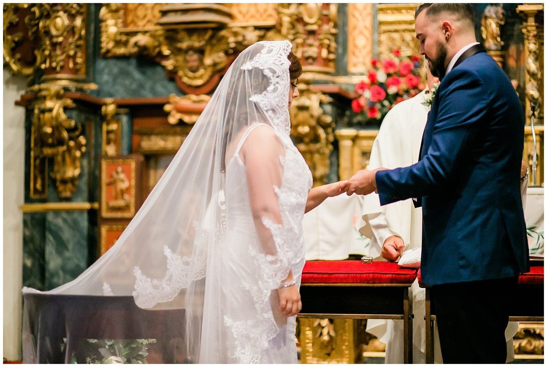  groom puts the ring on the bride’s finger at the altar 