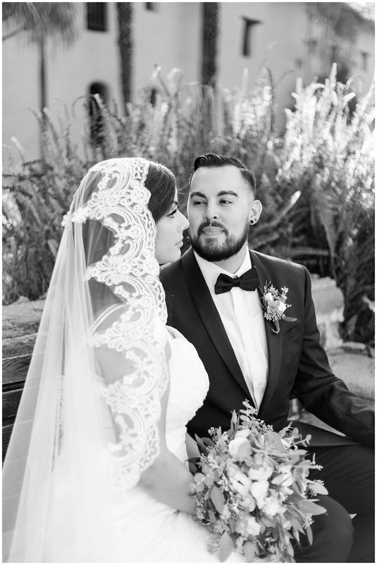  black and white photo of bride and groom sitting on a bench in front of the plants 