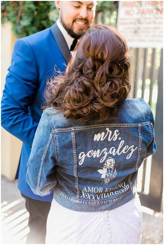  bride and groom holding hands and bride wears a jean jacket with mrs gonzales written on the back 
