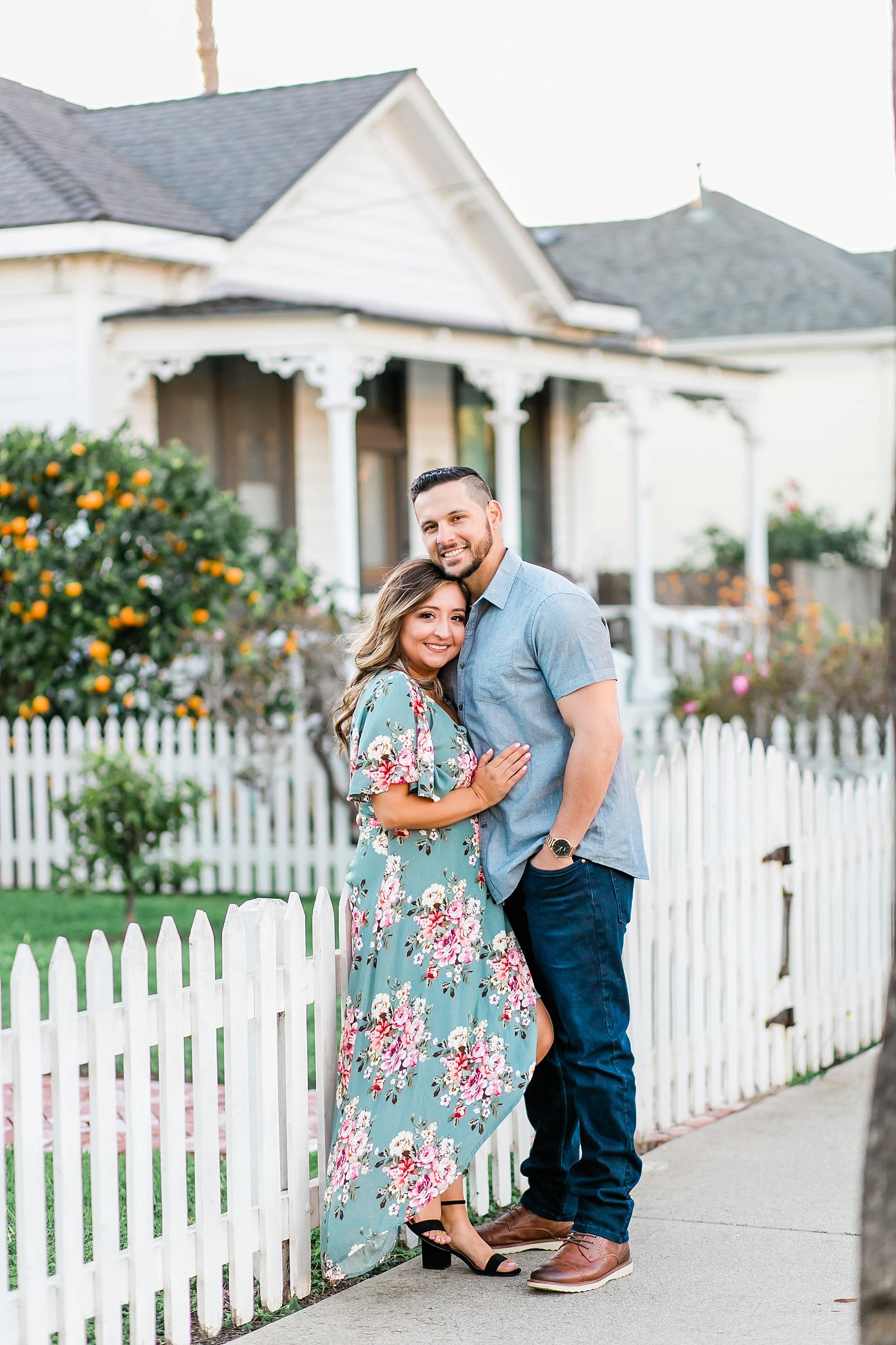  newly engaged couple embracing in front of the white picket fence 