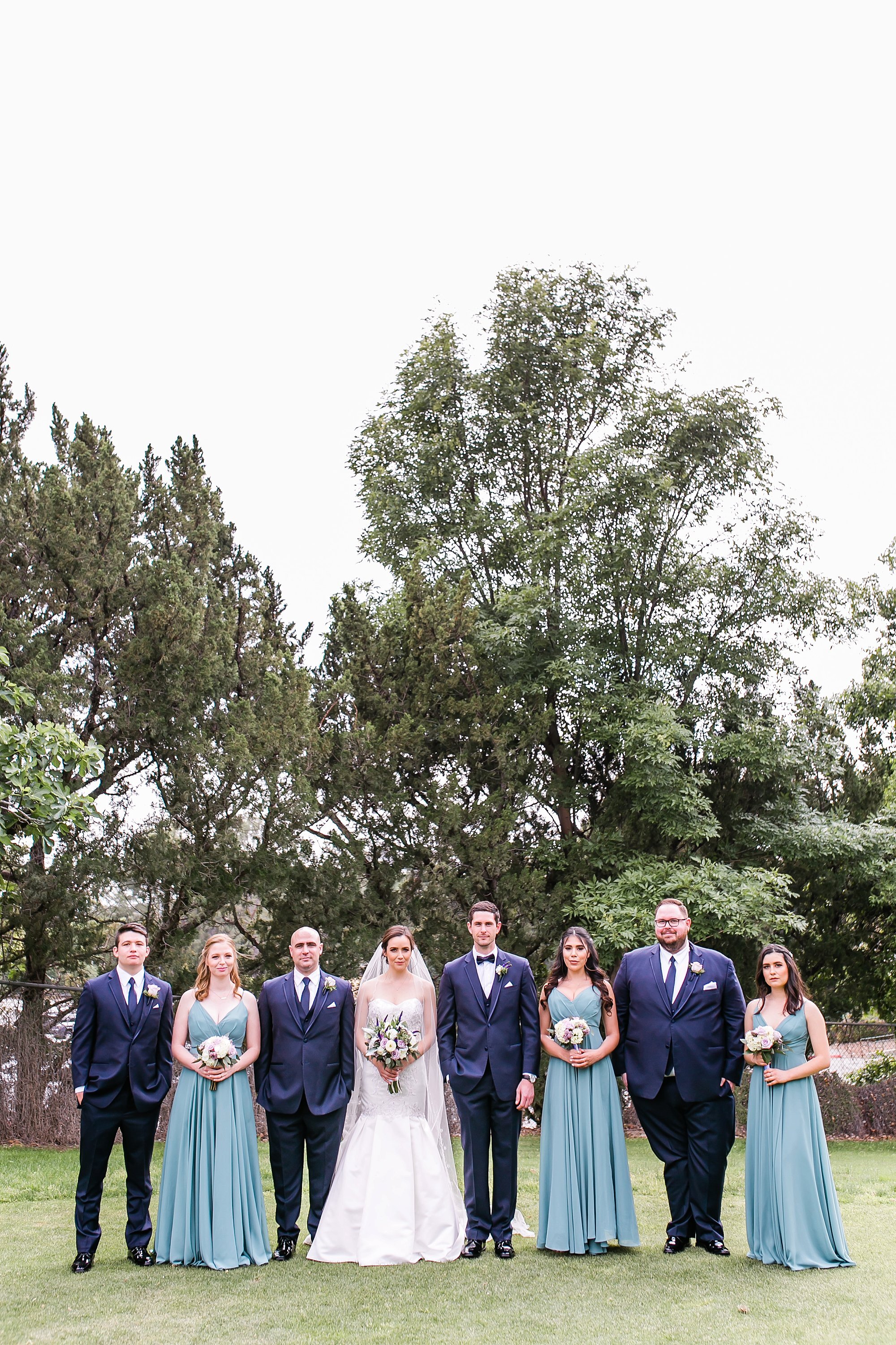  full wedding party in front of trees 