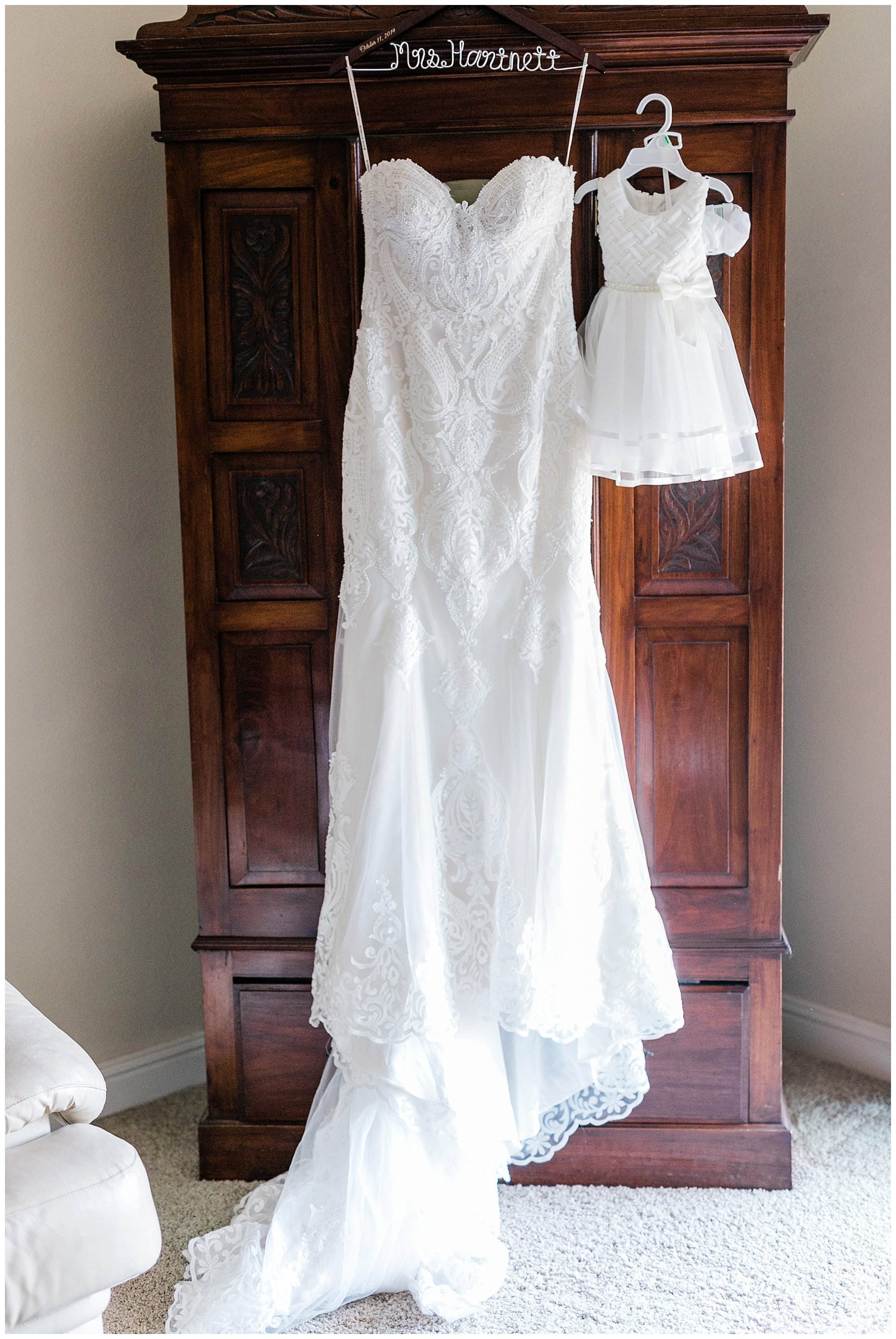  wedding gown and flower girl’s dress hanging on armoir 