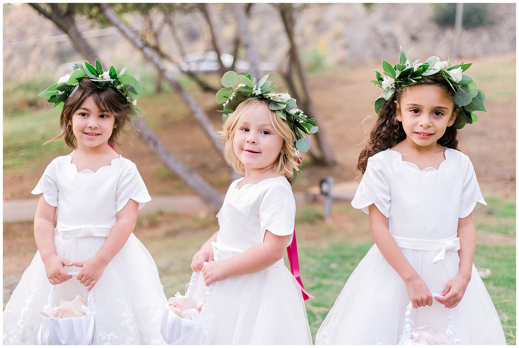  flower girls holding the baskets with the trees behind them 