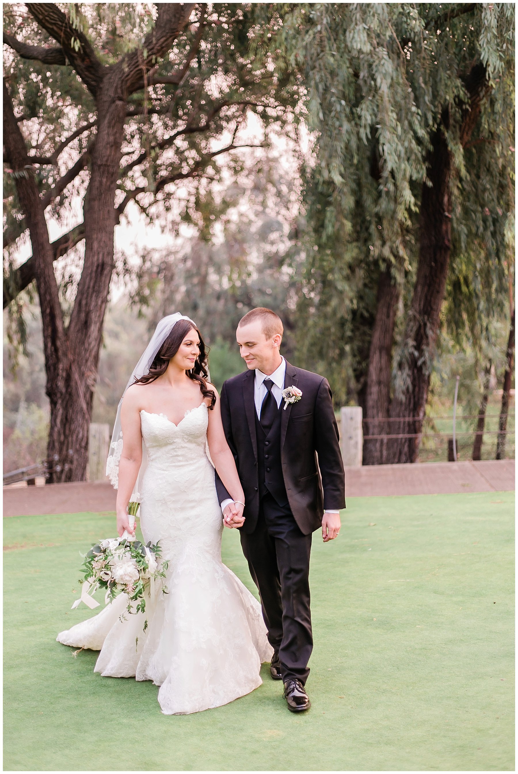  bride and groom walk through the golf course hand in hand looking at one another 