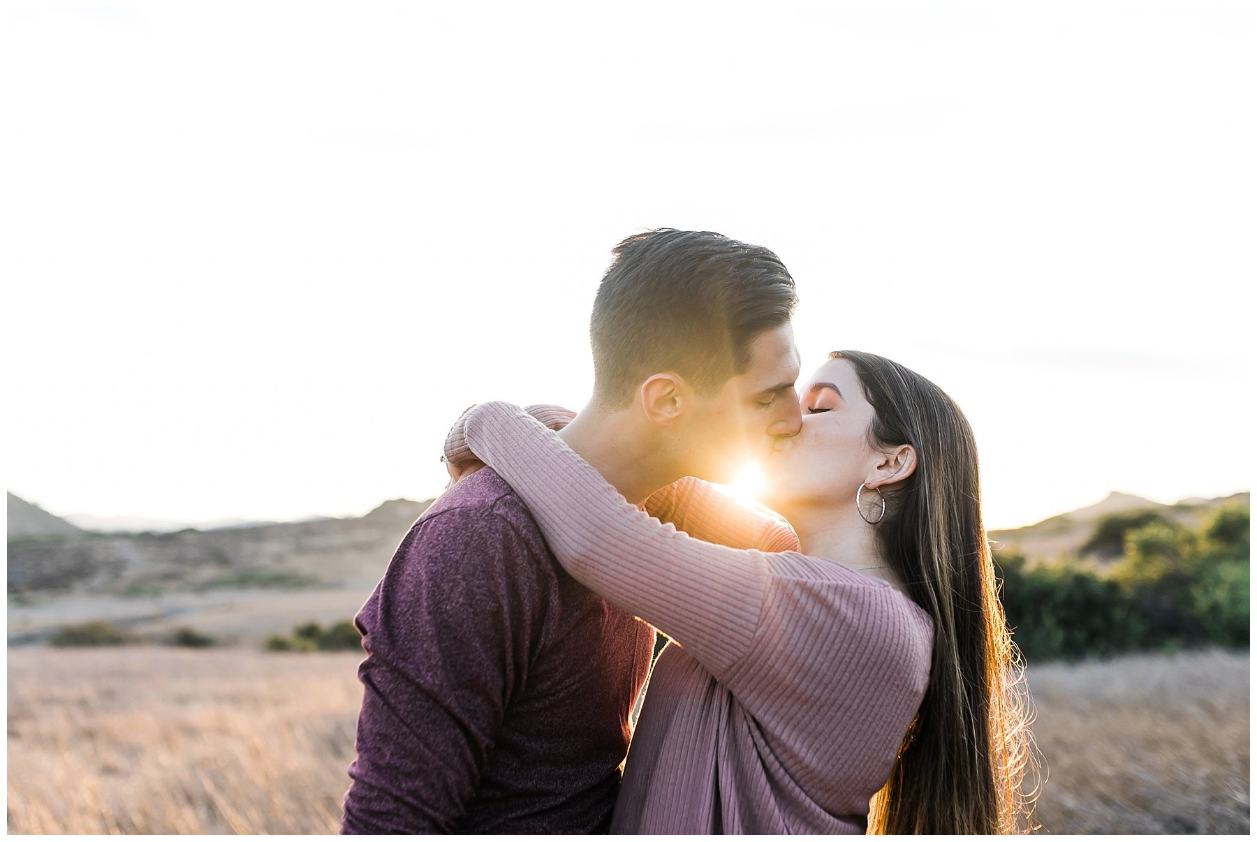  engaged couple kissing as sunlight streams through 