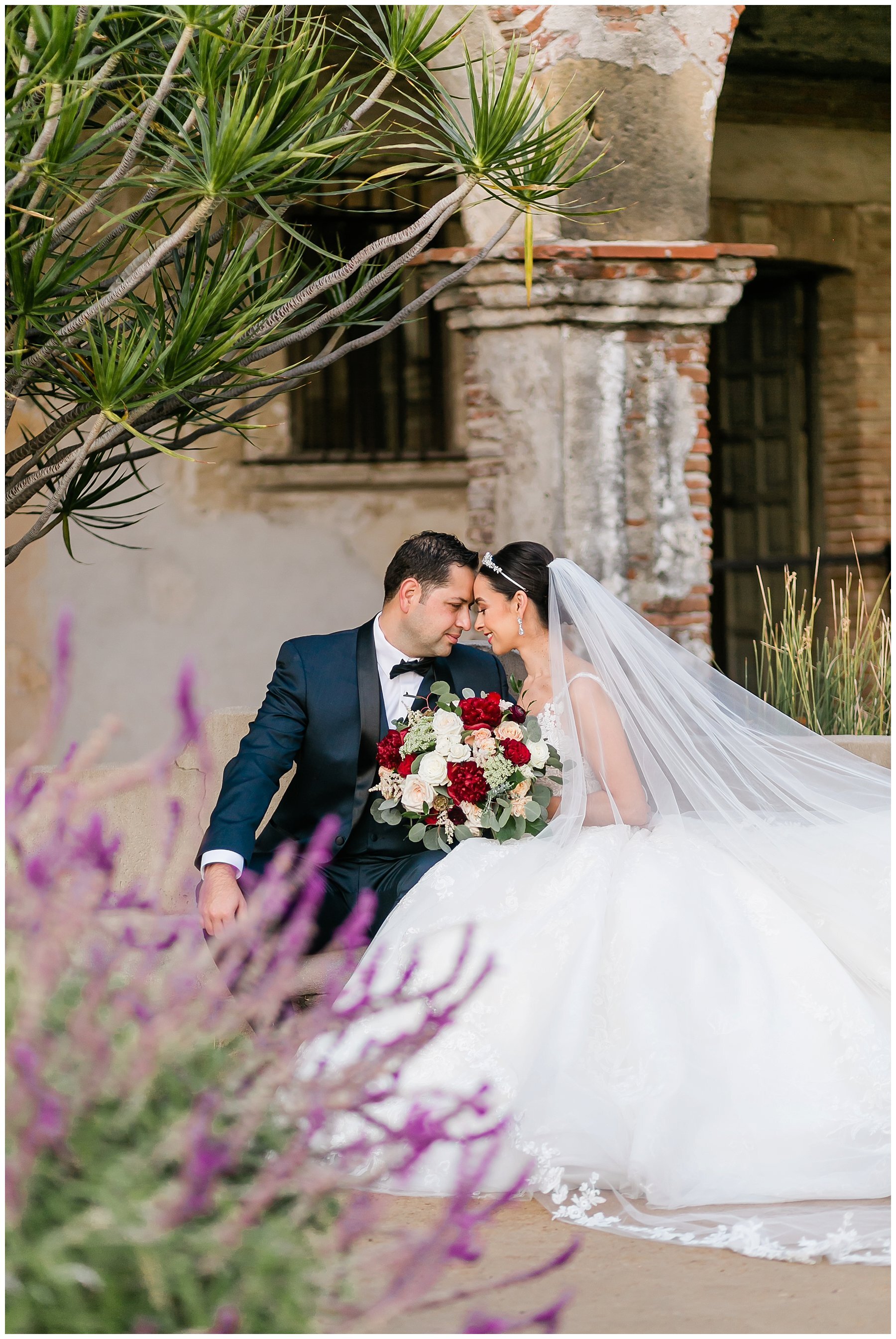 bride and groom touching foreheads in the courtyard with archways and greenery 