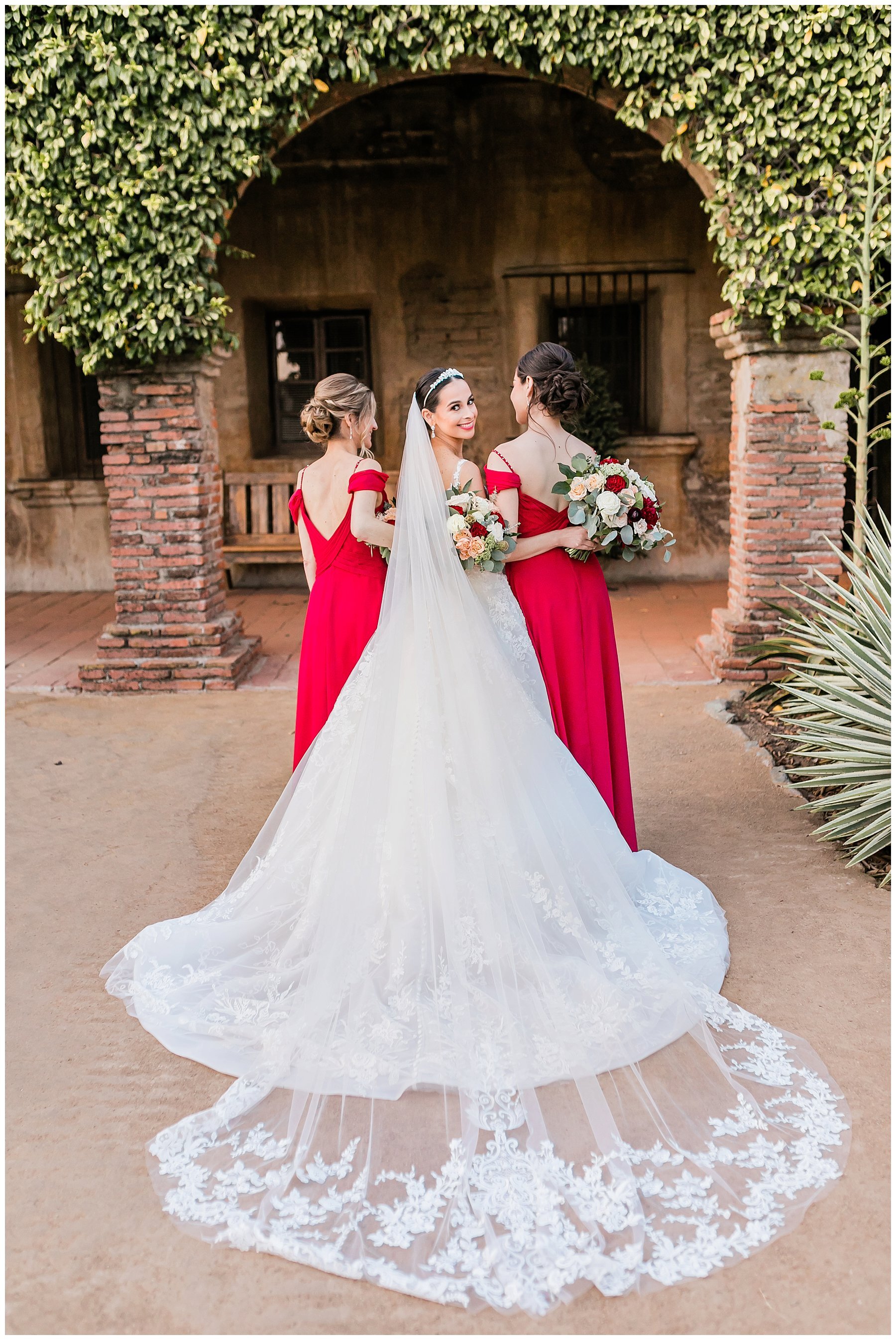  bride and bridesmaids in a red dress in front of an ivy covered arch 