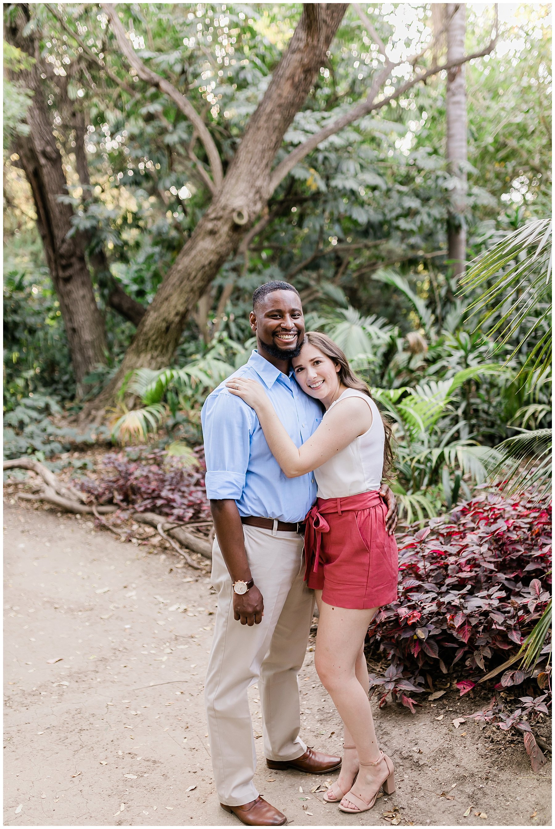  engaged couple standing on a path flanked by trees 