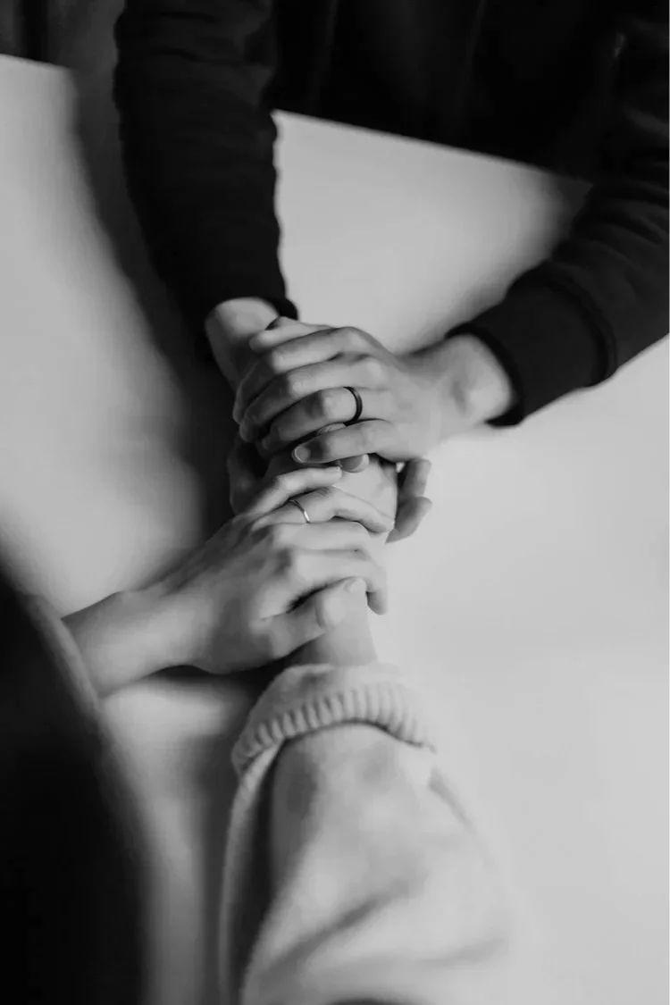 Black and white photo of multiple hands stacked together on a table, showing unity and teamwork.