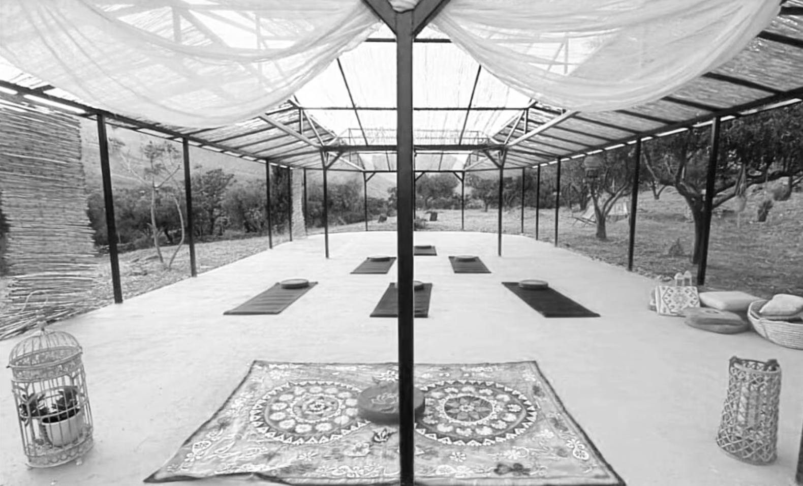 Outdoor yoga or meditation space with mats, pillows, rugs, and decorative lanterns on a covered patio surrounded by trees.