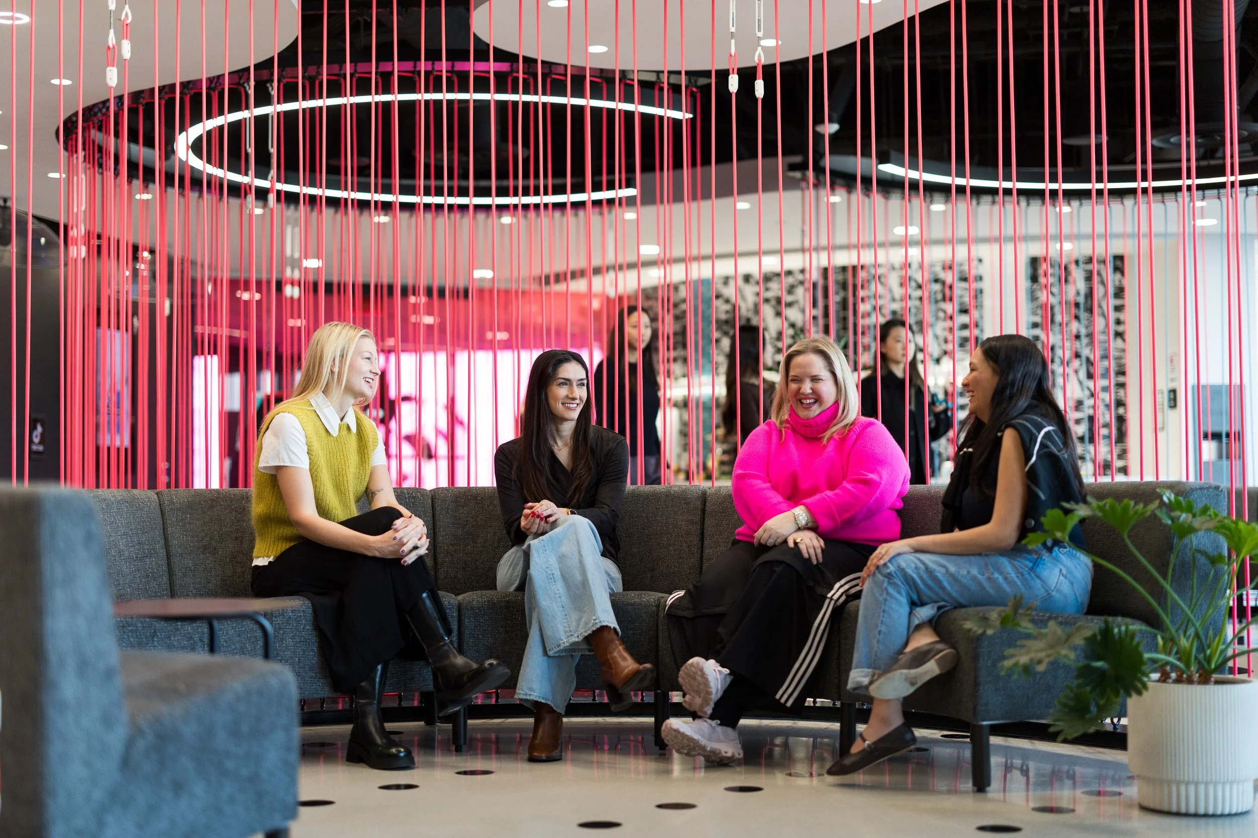 Corporate lifestyle photo of 4 young female employees dressed colorfully and sitting on a couch in one of the common areas of TikTok's NYC office