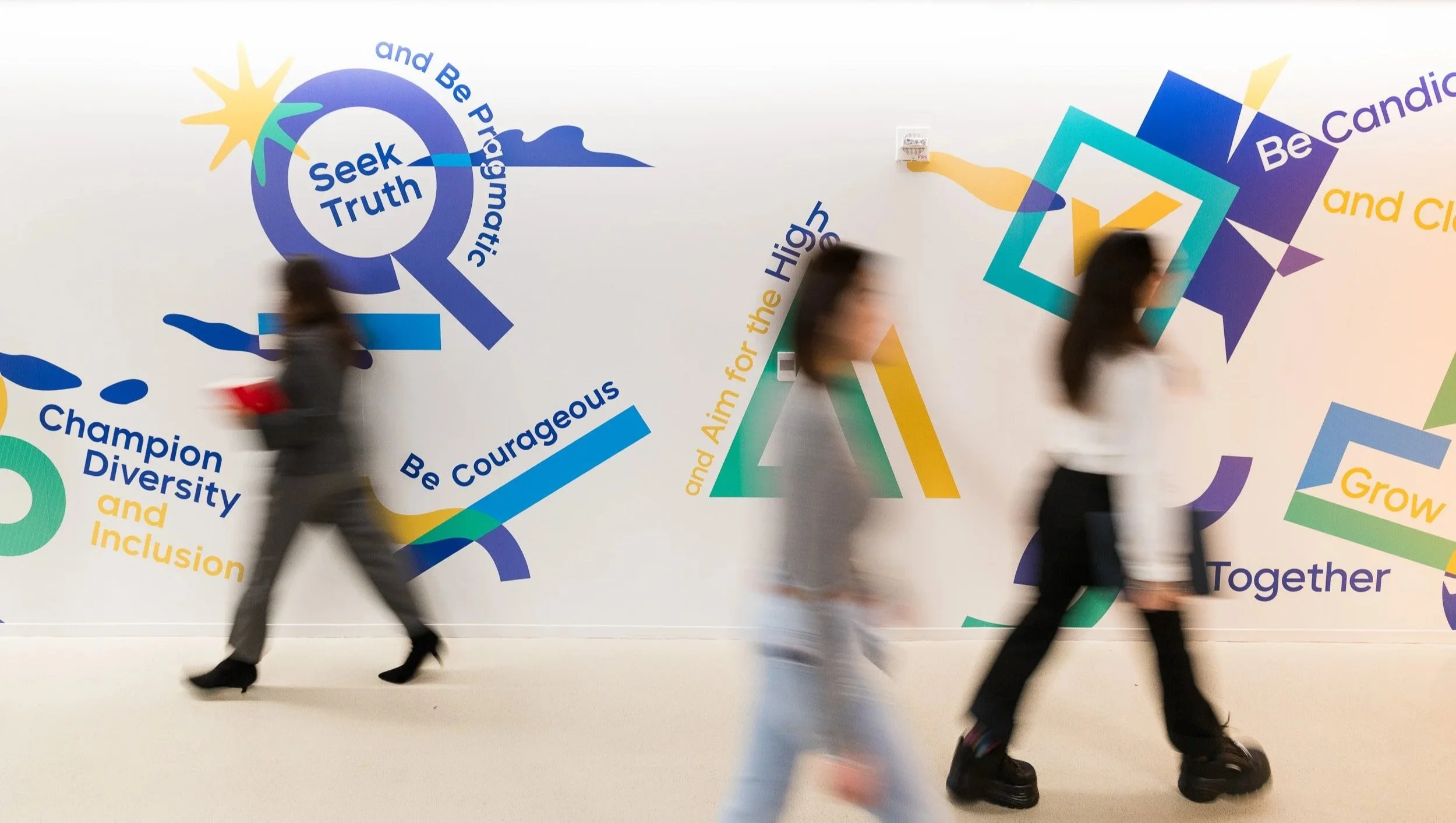 Corporate lifestyle photo showcasing 3 blurred figures in motion against a wall with TikTok's core values and principle's on it.