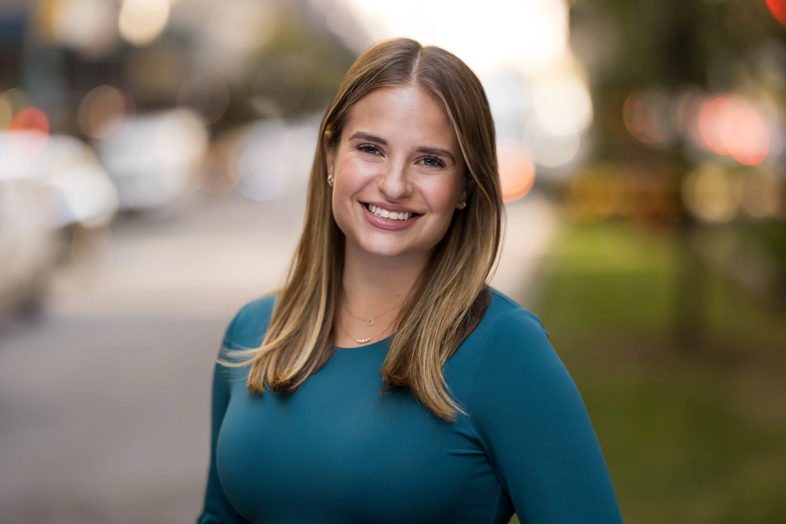 Modern corporate headshot of a young white female wearing a blue sweater smiling outdoors in NYC