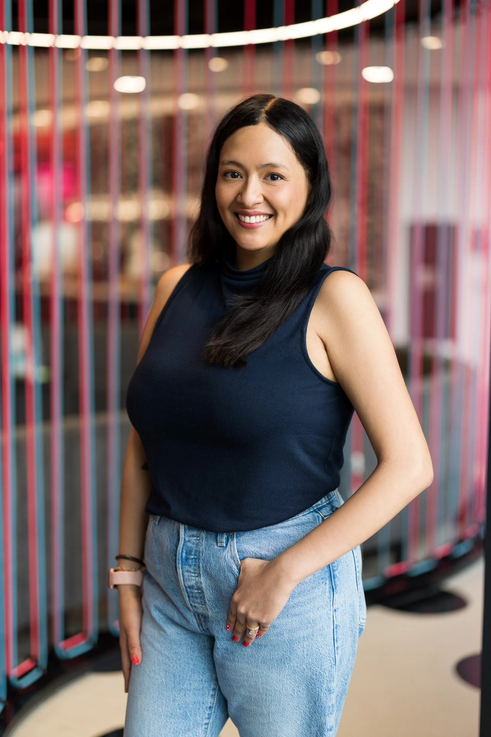 Modern corporate headshot of Latin woman smiling with her hand in her pocket against a colorful office background
