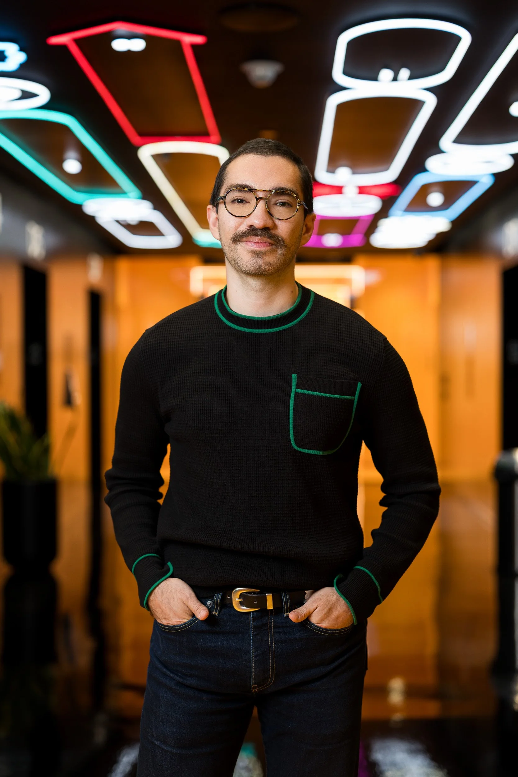 Corporate lifestyle portrait of young man posing in an orange hallways with neon lights on the ceiling
