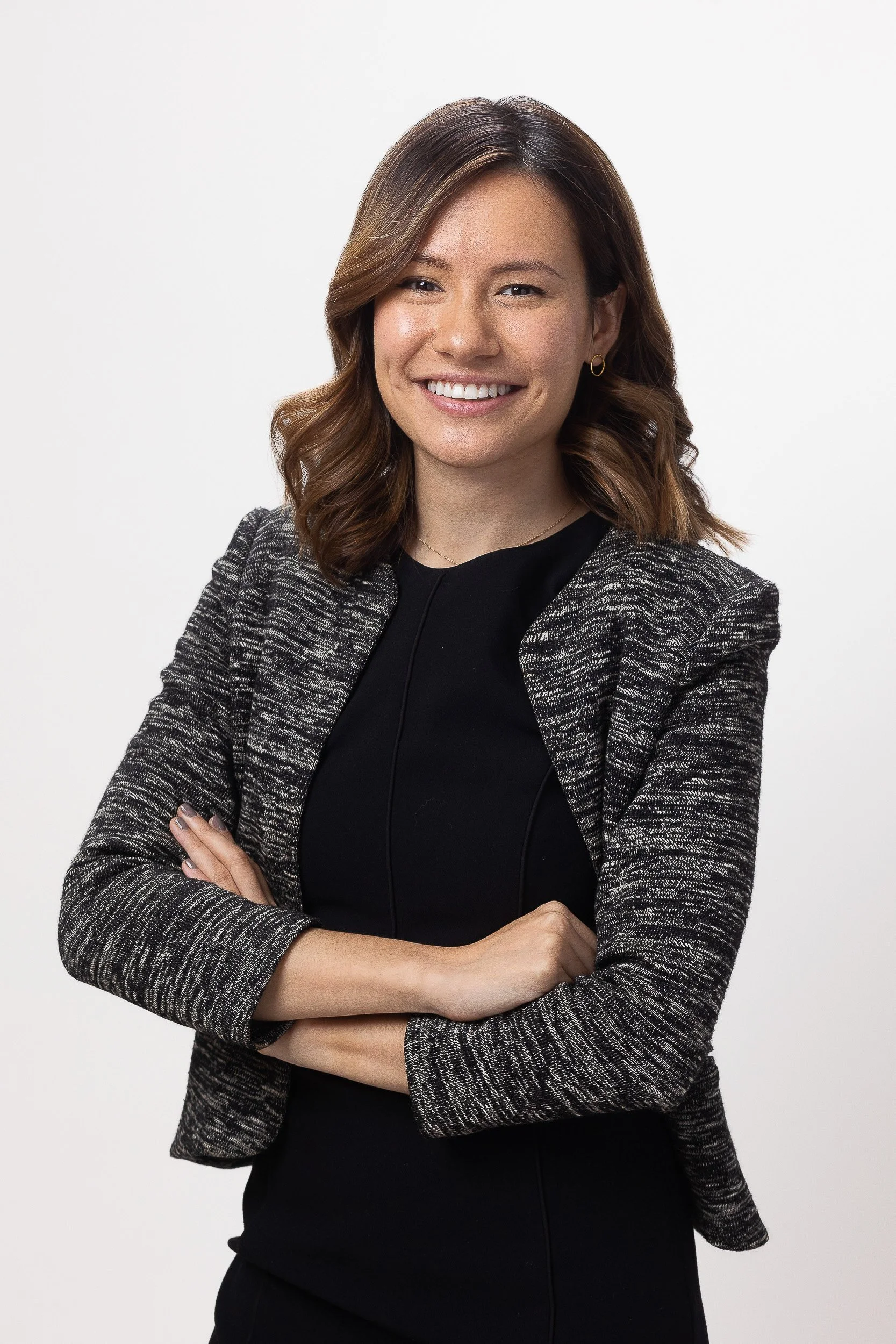 Professional headshot of a young Asian female smiling with crossed arms against a white studio background