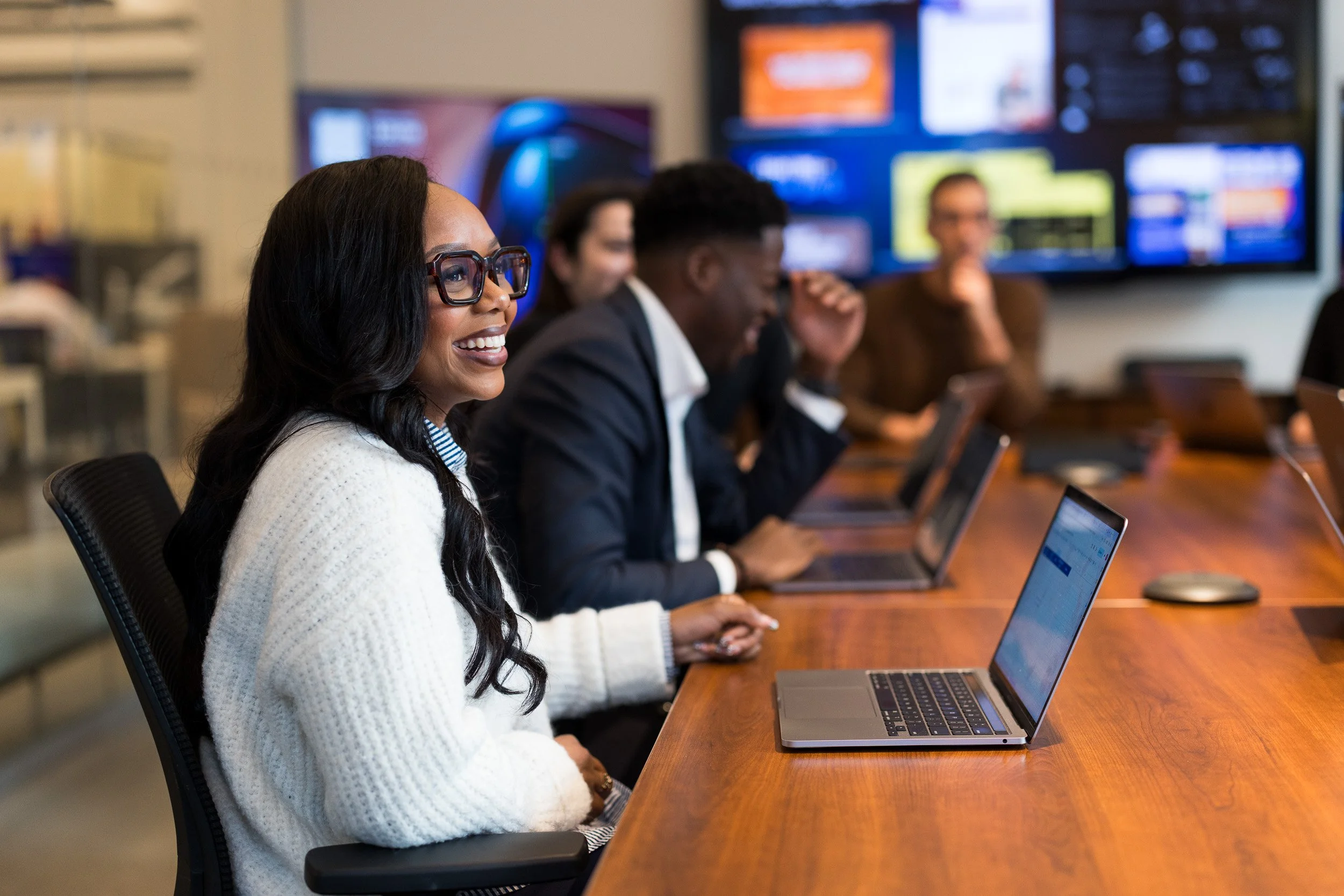 Corporate lifestyle photography showing a coworking scene of employees collaborating in a conference room of their NYC office, with the focus on a smiling female in front of her laptop.