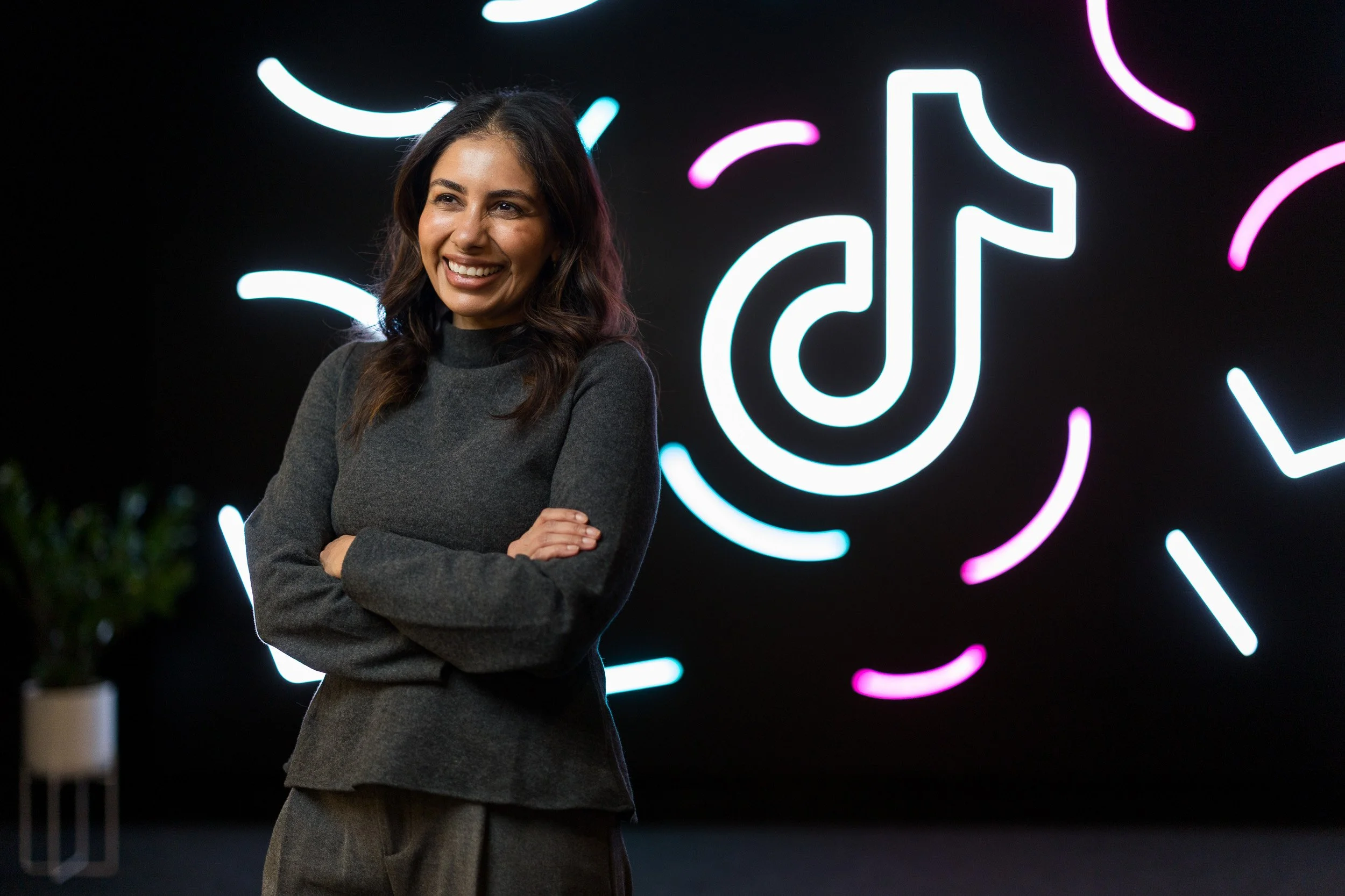 Corporate lifestyle portrait of a young female employee posing with the TikTok logo in neon lights in the background