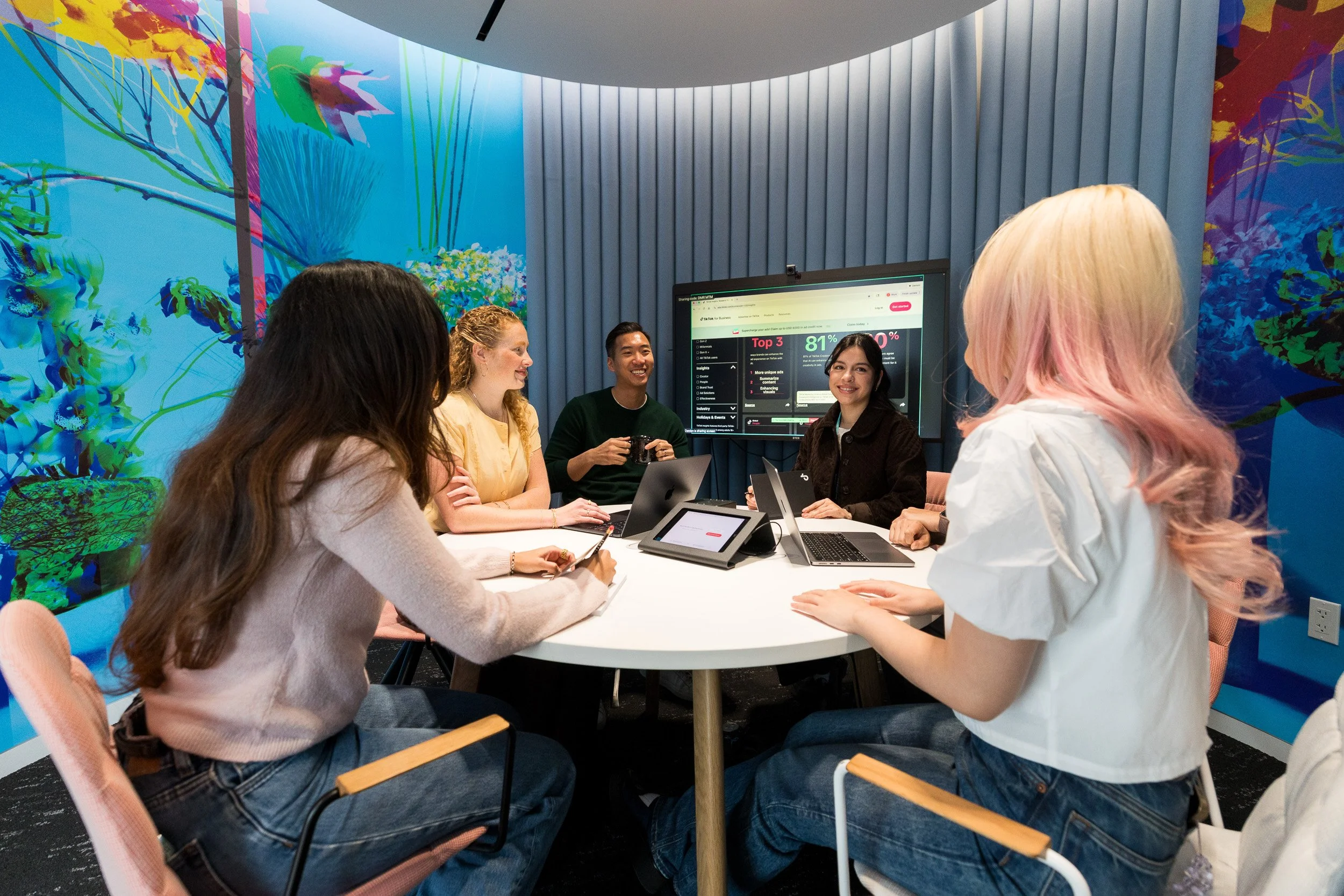 5 employees sitting in a small and colorful huddle room having a meeting at work