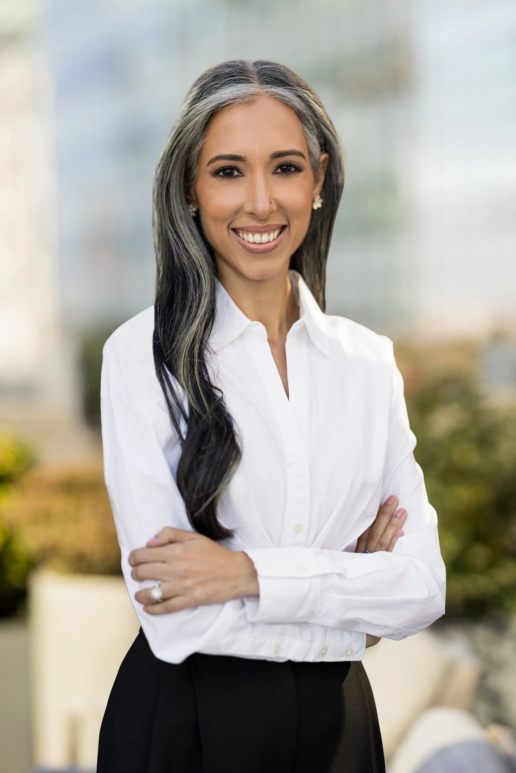 Professional headshot of an Indian woman wearing a white blouse with arms crossed outdoors in NYC