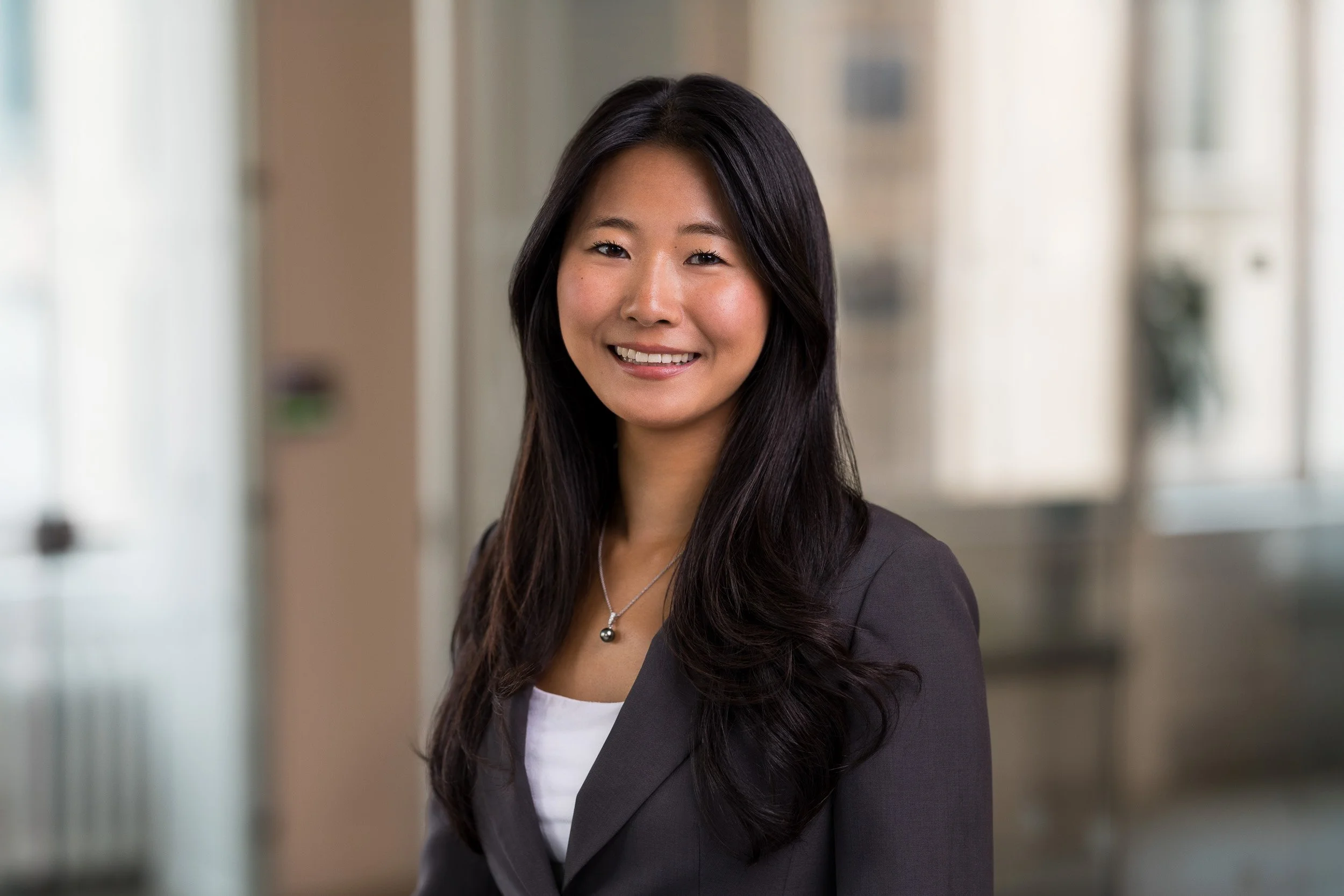 Modern corporate headshot of young Asian female employee with a blurred office background