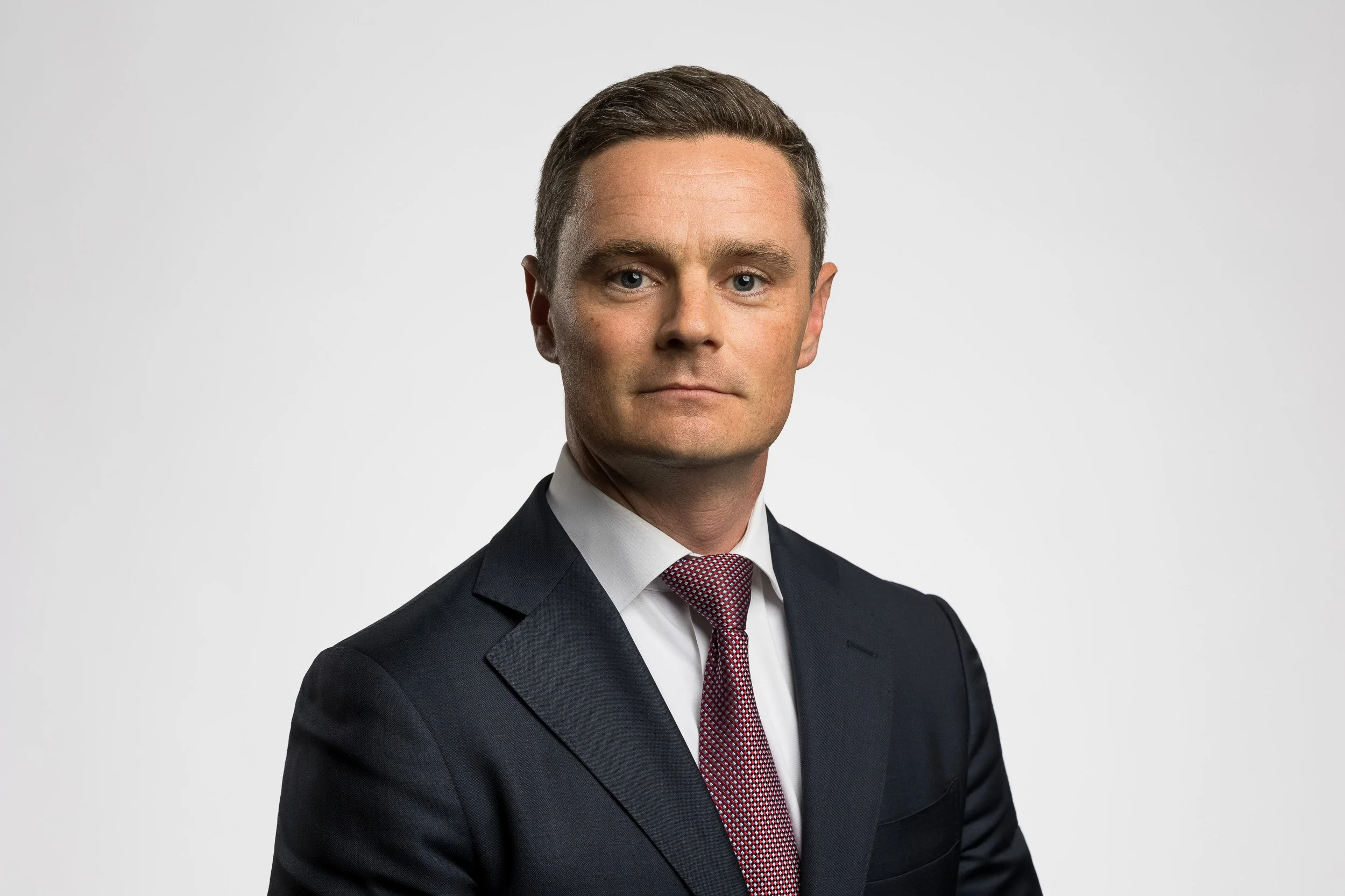 Studio headshot of middle-aged male wearing a suit and tie against a white backdrop.
