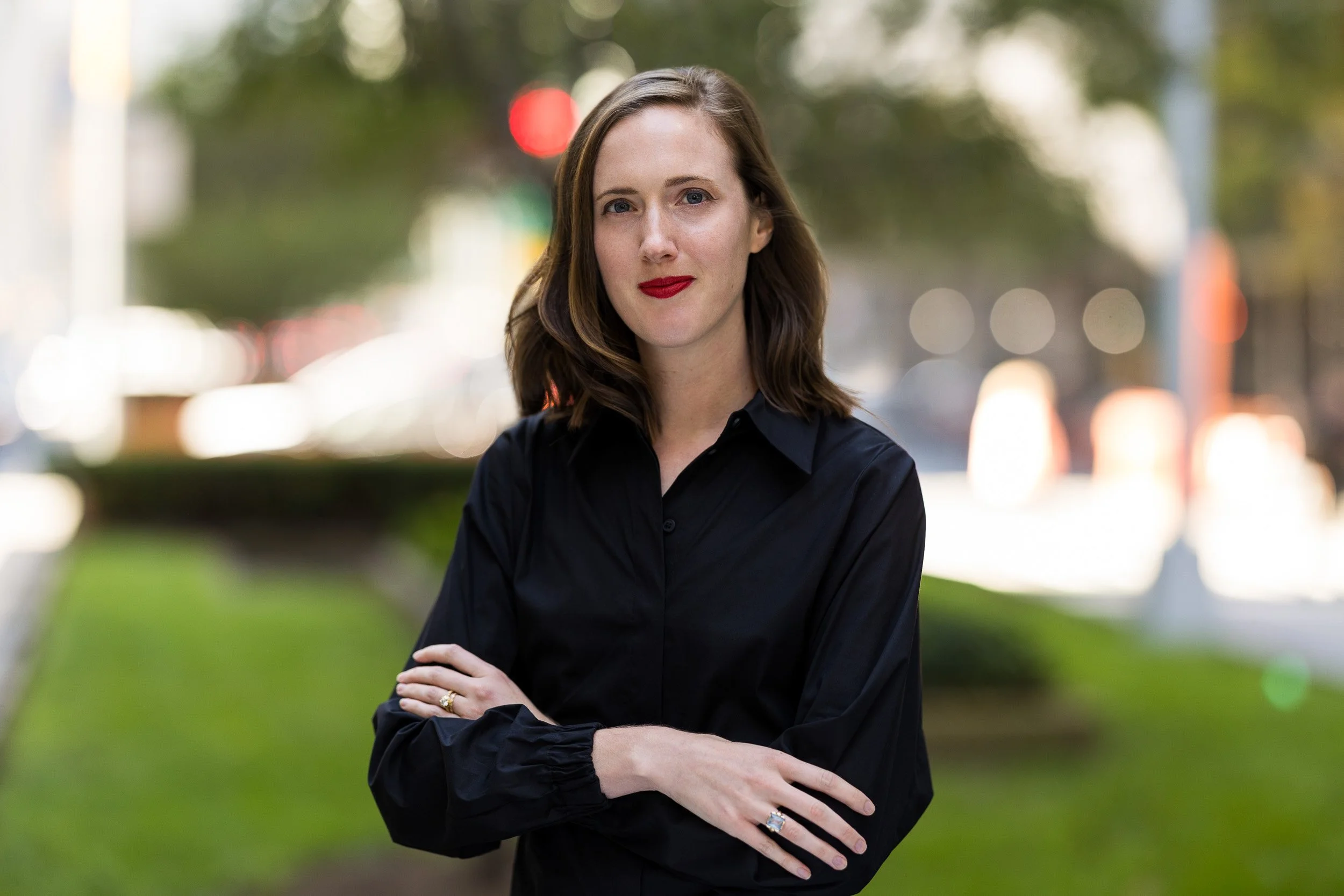 Outdoor corporate headshot of a woman in her 30's wearing a black blouse photographed outdoors with natural light in NYC