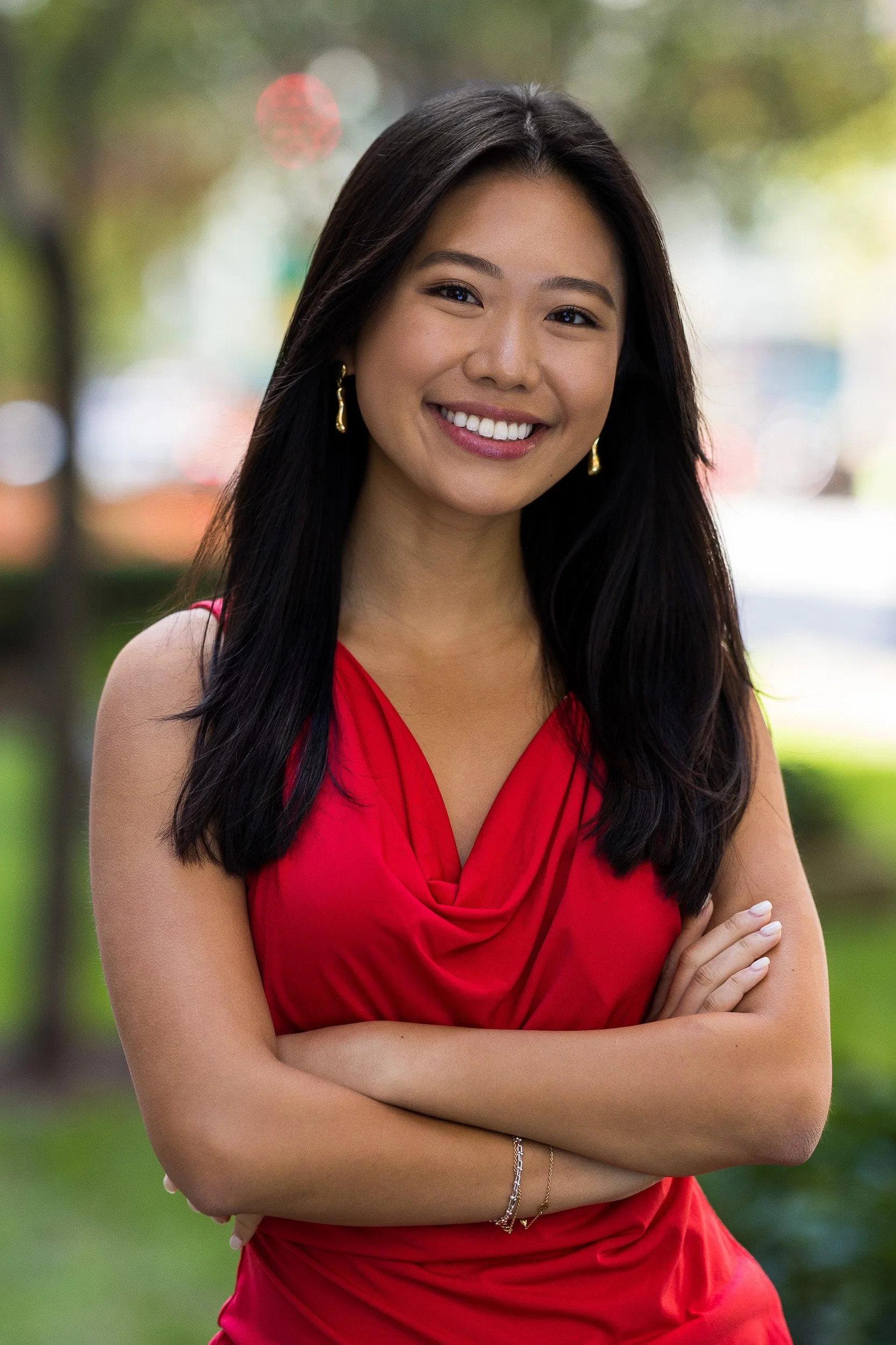 Modern female professional headshot of a young Asian woman in a red dress smiling with her arms crossed outdoors in NYC